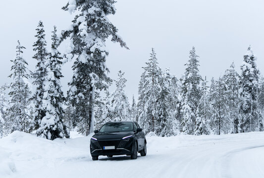 Modern black crossover car parked on a snowy road in a beautiful winter pine forest, scenic automotive travel concept, Lapland arctic landscape
