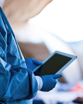 Gloved healthcare worker holding digital tablet inside bright clinical tent during patient intake with ample copy space and soft background blur