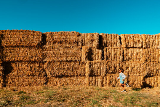 Little girl running by a huge hay bale stack