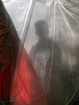 Clear vinyl window blurred silhouette mobile quarantine tent isolation translucent plastic red light clinical tension privacy screen extreme close up vertical composition