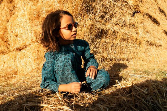 Little girl crouching in front of a huge hay bale stack