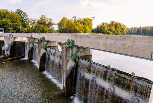 River weir with flap gates and waterfall in Augsburg, Germany, concrete dam on sunny autumn day with colorful trees, water management and flood control