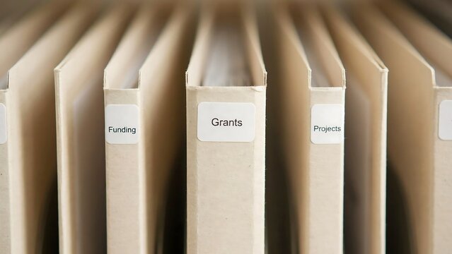 Close up of manila file folders standing in a row with labels for funding, grants, and projects visible on the tabs in an organized office setting
