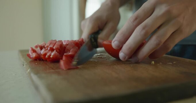 Close-up male hands cut tomato with knife on wooden cutting board. 4K 10-bit
