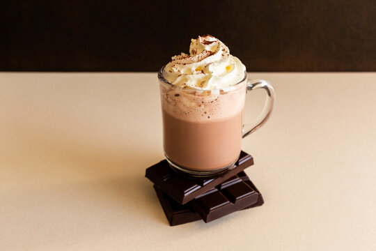 Chocolat chaud avec chantilly dans une tasse transparente pos&eacute;e sur des carreaux de chocolat