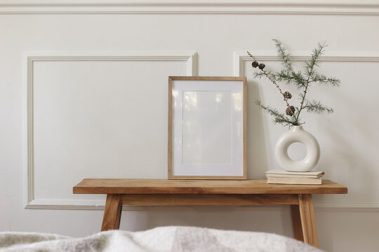 Minimalist Christmas Scandinavian Interior. Blank Wooden Picture Frame Mockup, White Ceramic Donut Vase with Pine Branches on Rustic Wood Console Table. Neutral Nordic Home Decor, Winter Living Room