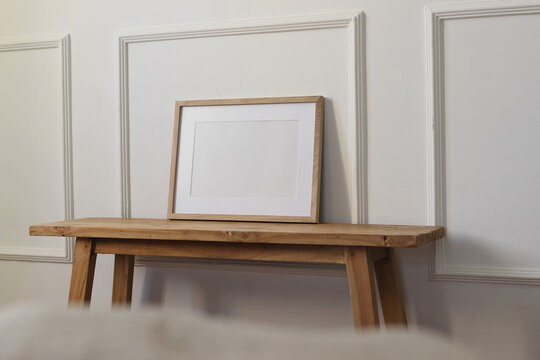 Blank Wooden Picture Frame Mockup. Rustic Oak Console Table Against Elegant White Wall. Minimalist Scandinavian Interior, Horizontal Sparse Poster Template, Neutral Nordic Home Decor. Blurred blanket
