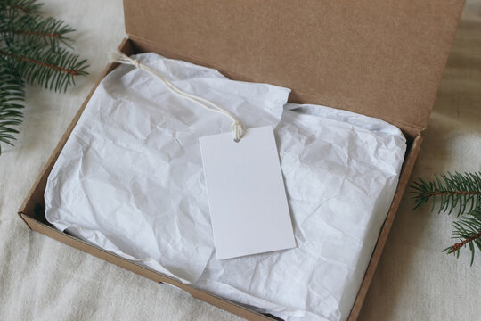 Blank White Gift Tag Mockup. Cotton String. Crumpled Tissue Paper Open Kraft Cardboard Gift Box. Minimal Christmas Packaging, Sustainable Branding, Eco Friendly Wrapping. Fir Tree Branches Flatlay top