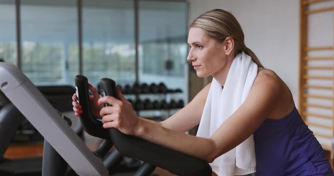 Focused woman training on stationary exercise bike at gym. Cardio workout