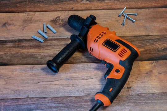 Orange corded electric drill, screws and wall plugs arranged on a rustic wooden workbench
