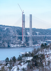 Winter engineering scale is revealed by tall pylons, crane and converging cables on the new E18 Grenlandsbrua above a Norwegian fjord for construction and transport development themes. © Nimbus Works