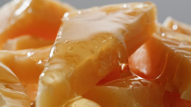 Cheese with honey close up, golden honey pouring over sliced orange cheddar cheese pieces, gourmet appetizer and wine snack for cafe and restaurant