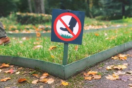 Rule violation concept: A person stepping near a "Keep off the grass" warning sign in an autumn park.