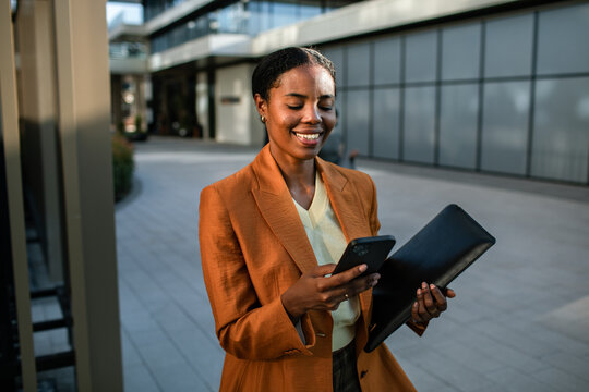 Businesswoman smiling at smartphone while holding portfolio outdoors