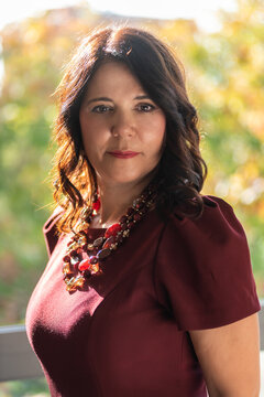 A sophisticated portrait of a mature woman wearing a stylish burgundy dress and a beaded necklace against a soft, bright background