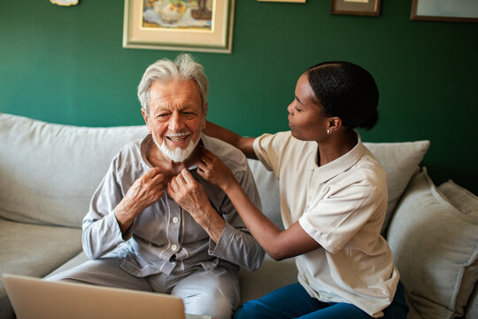 Caregiver helping senior man button pajamas at home