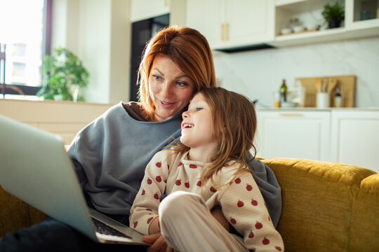 Mother and daughter cuddling on sofa with laptop