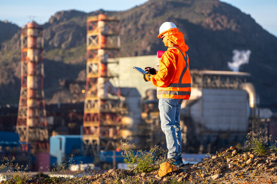 Mining engineer in safety gear reviewing a tablet at an industrial site, assessing operations