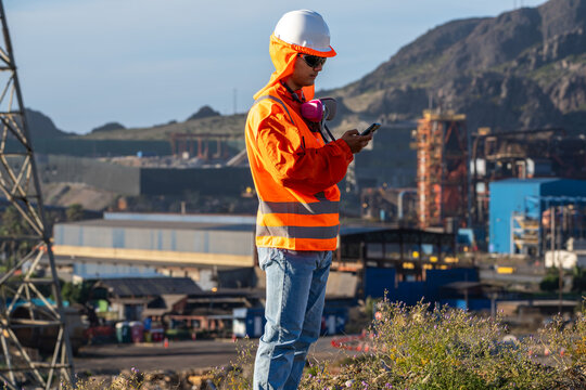 Industrial worker in protective gear checking a smartphone at an outdoor mining facility