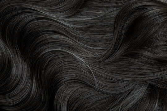 Brunette or black hair. Female long dark hair in black. Beautifully laid curls. Closeup texture in a dark key. Hairdressing, hair care and coloring. Shading gray hair. Background with copy space.