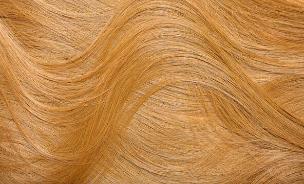 Red hair close-up as a background. Women's long orange hair. Beautifully styled wavy shiny curls. Hair coloring bright shades. Hairdressing procedures, extension.
