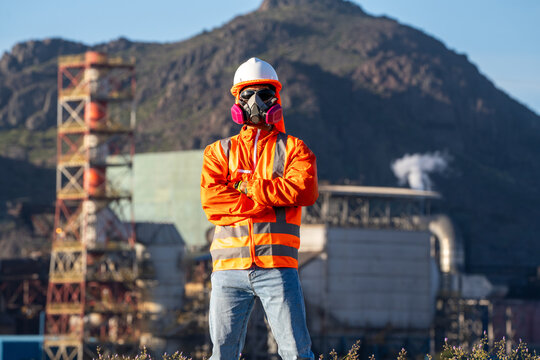 Industrial worker wearing a respirator and hard hat, standing at an outdoor plant