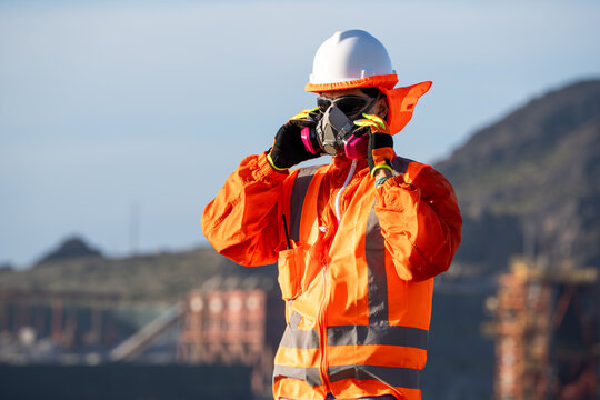 Industrial worker adjusting a respirator, wearing high-visibility safety gear at an outdoor site