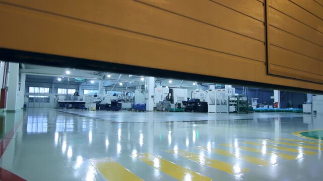 Garage door opening reveals modern factory floor. Gate rising machinery hall.