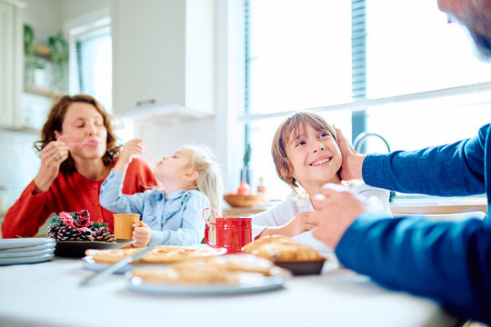 Family sharing breakfast at a kitchen table, parents and children smiling over pastries and drinks in warm morning light at home