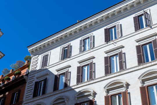 White neoclassical building facade with brown wooden shutters against a deep blue sky in central Rome, Italy