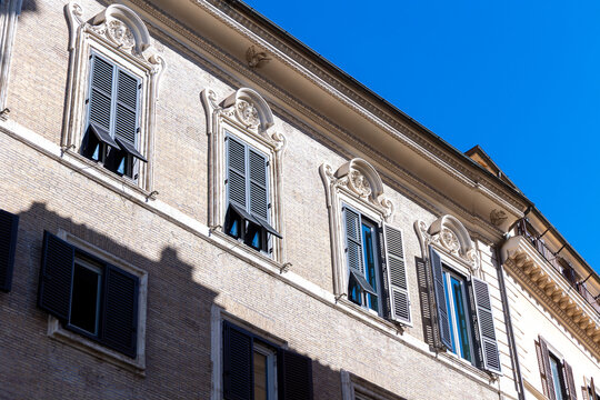 Low angle view of ornate Roman building facade with shuttered windows against a clear blue sky in Rome, Italy