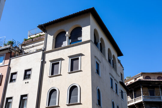 Low angle view of traditional Roman building facade with arched windows and terracotta roof against blue sky