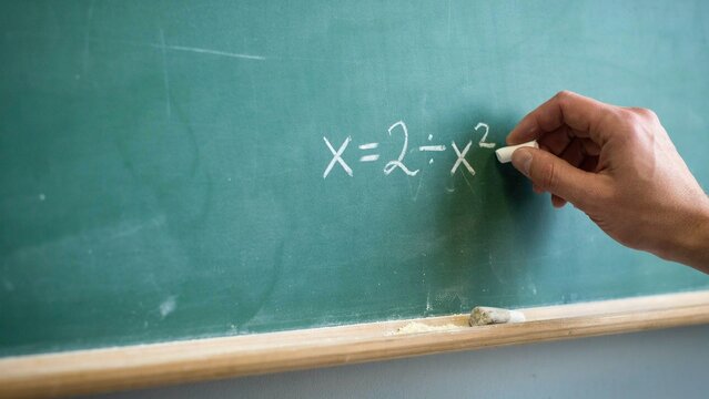 Hand writing a mathematical equation on a green chalkboard with white chalk