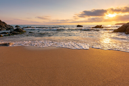 golden cloudy sunrise above the calm sea waters. waves crashing the sandy beach. clear horizon. changing windy weather