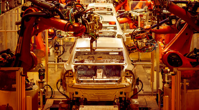 Automotive factory assembly line, industrial robotic arms spot welding car body-in-white shell, automated automobile manufacturing plant with welding sparks 