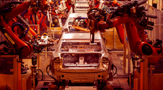 Automotive factory assembly line, industrial robotic arms spot welding car body-in-white shell, automated automobile manufacturing plant with welding sparks 