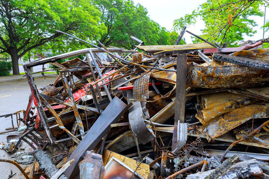 Large heap of scrap metal, wooden pieces fills street near trees under heavy hurricane in city.