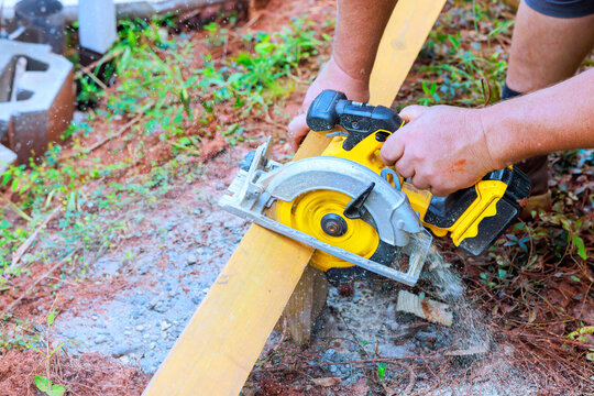 Contractor operates circular saw on wooden plank in construction site dust wood shavings fill air.