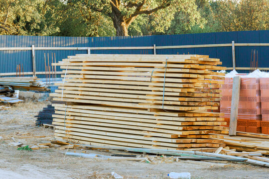 Workers stack wooden planks at construction site during work, tools materials surround area.