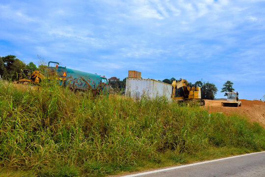 Several construction machines are parked near dirt mound beside road for highway junction expansion