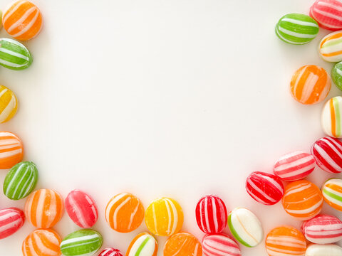 Colorful old fashioned striped hard candies arranged around the edges of a white background, creating a cheerful vintage candy frame with generous copy space for text or advertising.