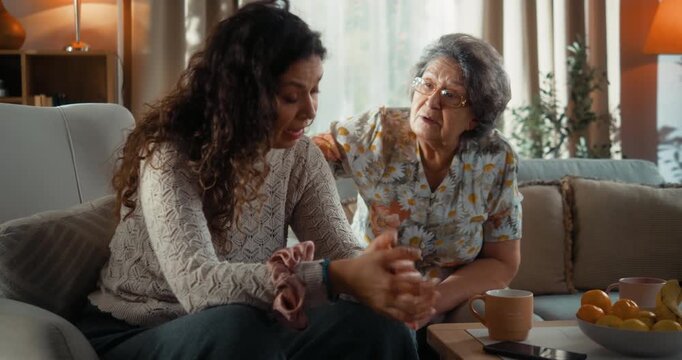 Senior mother talks to and advises her upset adult daughter during an emotional family conversation at home.