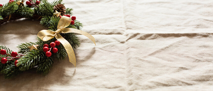 A festive evergreen wreath decorated with red berries and a gold ribbon rests slightly on wrinkled white paper.