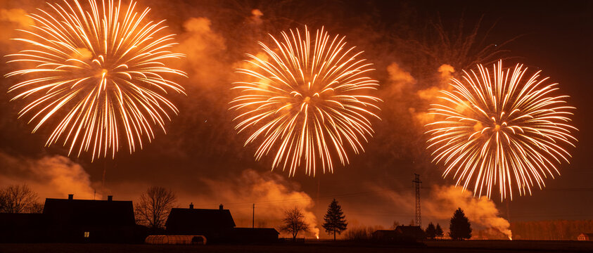 Bright golden fireworks exploding in the night sky above silhouetted houses during a celebration.