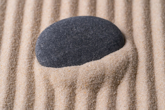 Black zen stone resting on raked sand meditation garden
