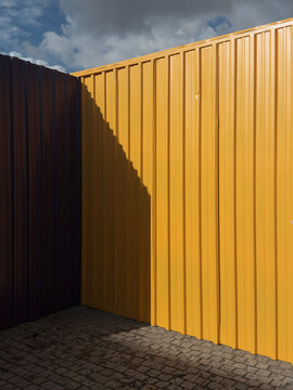 Sunlit yellow metal container wall with shadow under sky