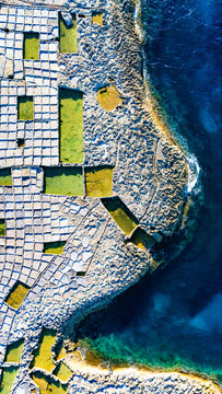 Top-down aerial view of the Xwejni salt pans with green pools along the rocky coastline of Gozo, Malta