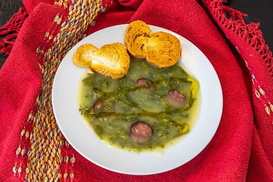Traditional Portuguese caldo verde soup with chouri&ccedil;o sausage, olive oil and toasted bread, top view