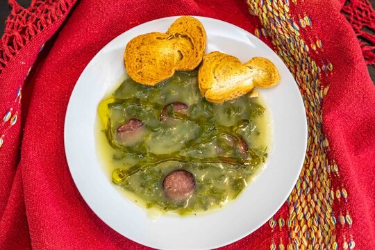 Traditional Portuguese caldo verde soup with chouri&ccedil;o sausage, olive oil and toasted bread, top view