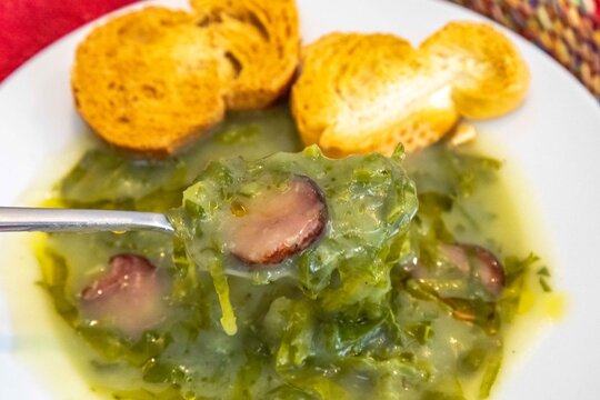 Traditional Portuguese caldo verde soup with chouri&ccedil;o sausage, olive oil and toasted bread, top view
